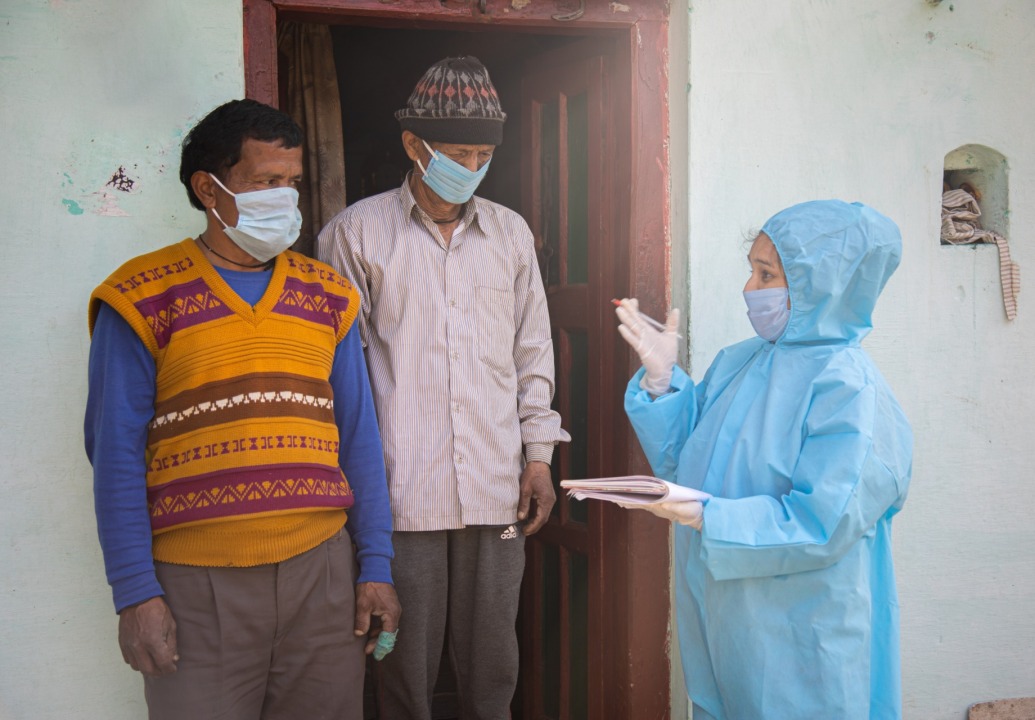 health-worker-PPE-talks-to-two-men