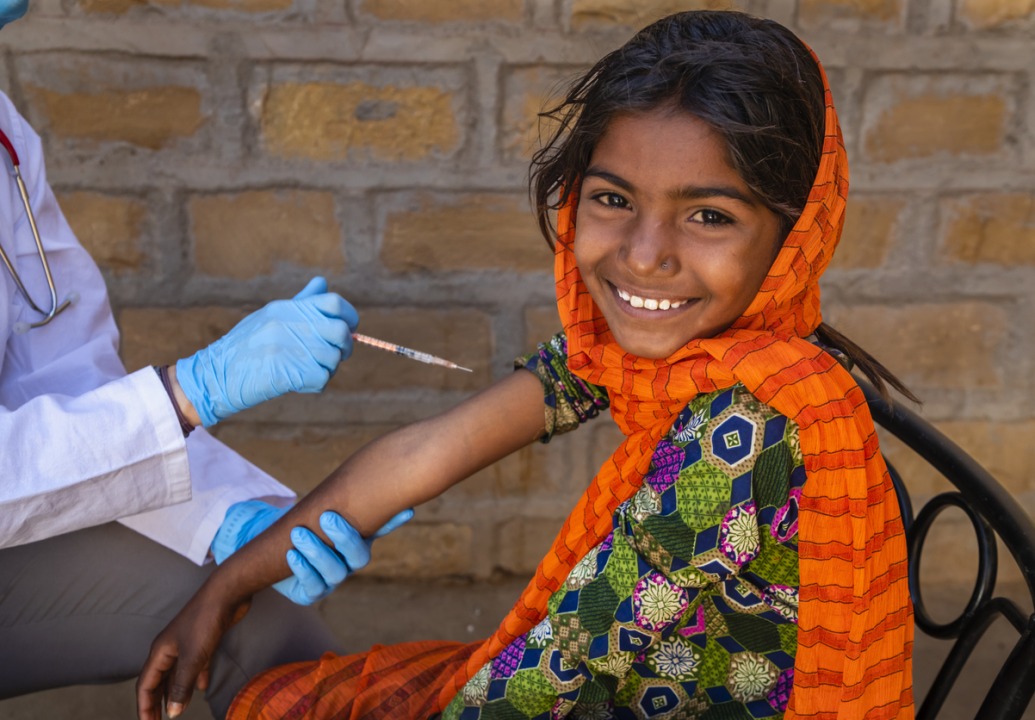 Female caucasian doctor vaccinating young Indian girl in small village, Rajasthan, India