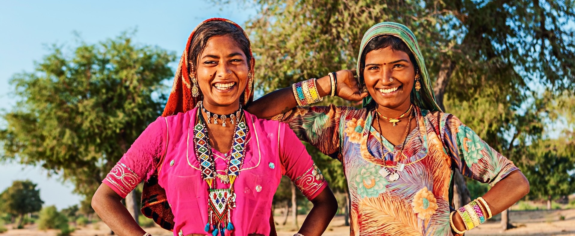 Two Indian women smiling at the camera with colorful dresses