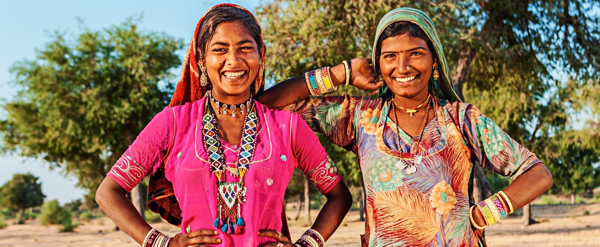 Two Indian women smiling at the camera with colorful dresses