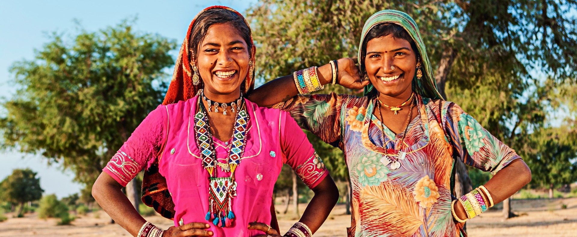 Two Indian women smiling at the camera with colorful dresses